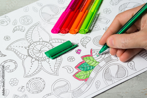 Woman coloring the coloring book for adults with abstract patterns, colored pens, antistress painting