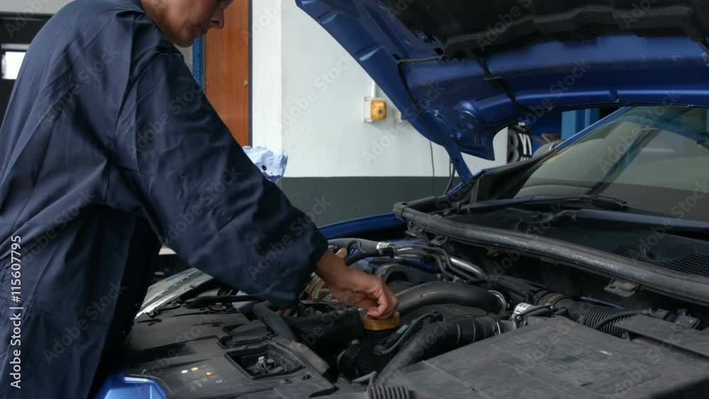 Female mechanic checking oil in the engine in the garage Female mechanic checking oil in the engine in the garage
