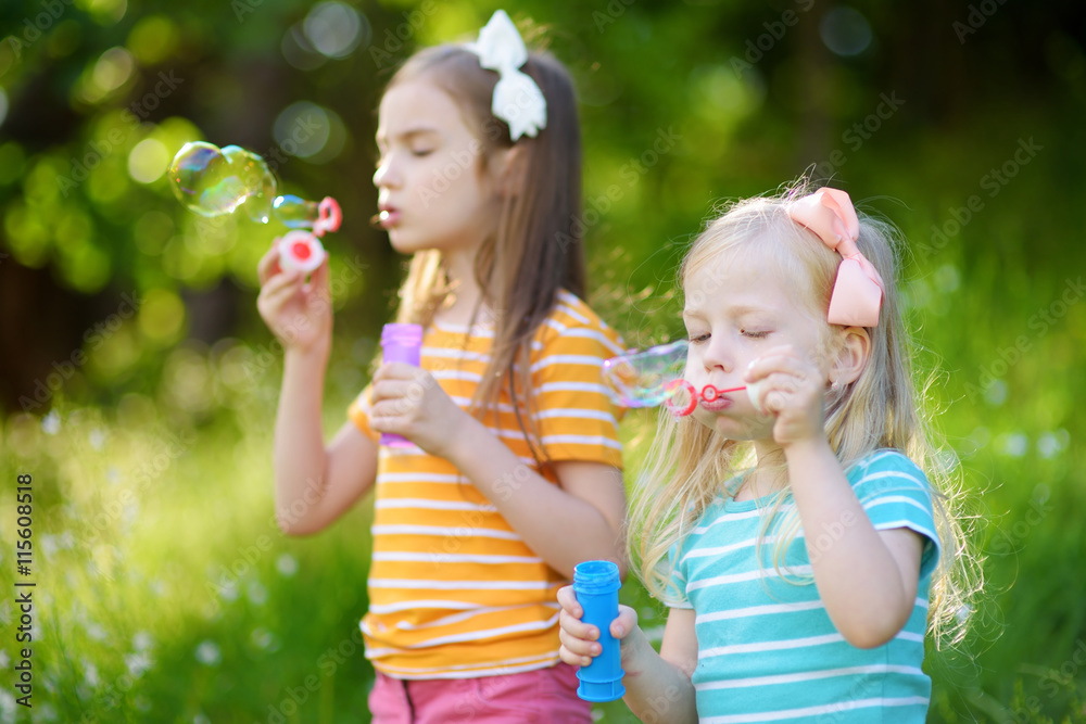 Two funny little sisters blowing soap bubbles outdoors