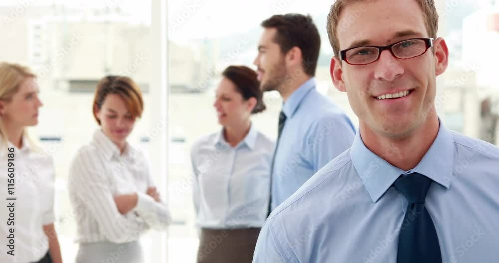 Businessman smiling at camera with colleagues behind him in the office Businessman smiling at camera with colleagues behind him in the office