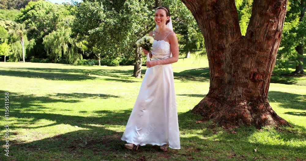Excited bride holding a bouquet in the park smiling at camera Excited bride holding a bouquet in the park smiling at camera