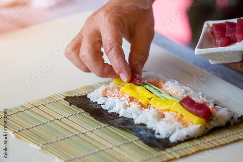 Hand puts piece of fish. Raw fish and white rice. Tuna for hosomaki rolls. Preparation of sushi in restaurant.