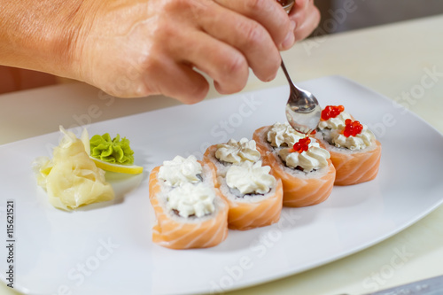 Spoon puts caviar on sushi. Small spoon in man's hand. Uramaki rolls with red caviar. Key ingredient for a delicacy.