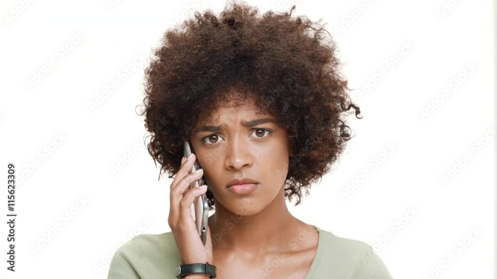 Upset young beautiful african girl speaking on phone over white background. Upset young beautiful african girl speaking on phone over white background.