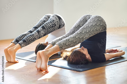 Two young women doing yoga asana plow pose photo