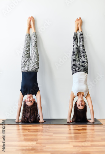 Photo Two young women doing yoga handstand pose