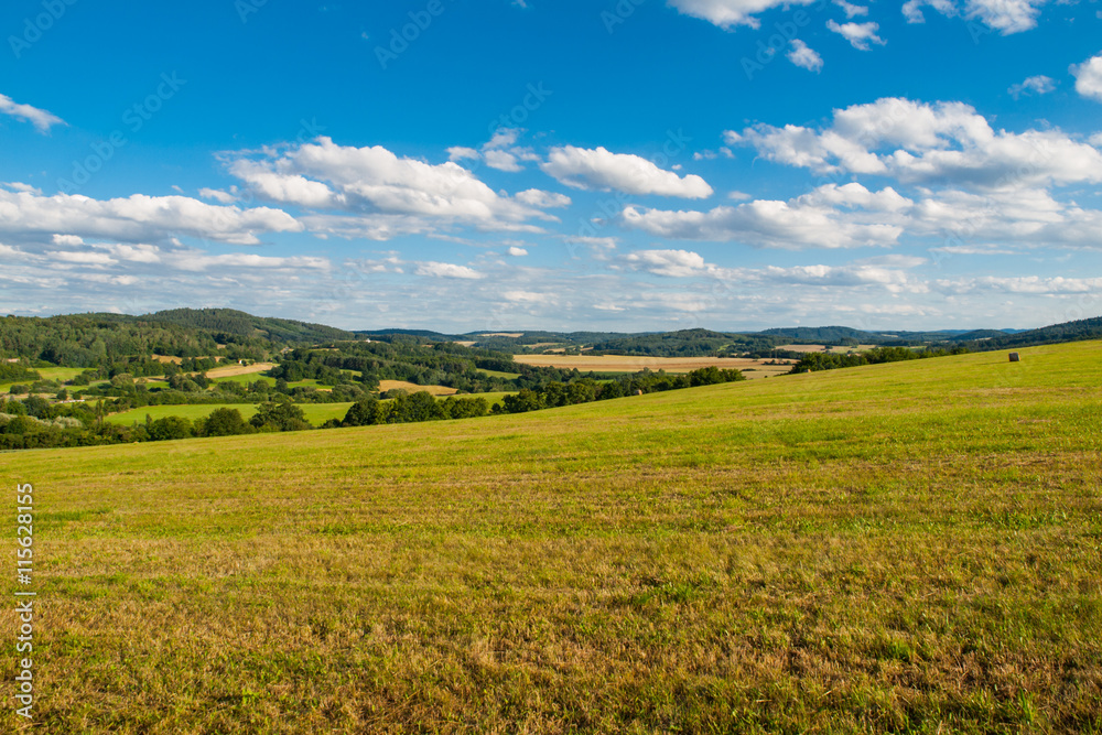 Summer hilly landscape withe green field, forests, blue sky and white clouds, Central Bohemia, Czech Republic
