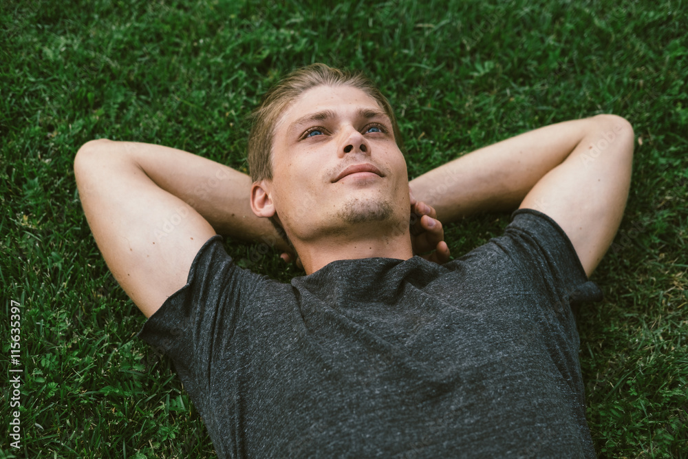 Attractive Young Man Lying with Both Hands Resting Behind his Ne - obrazy, fototapety, plakaty 