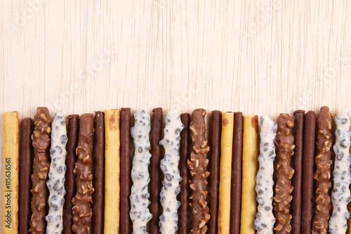 Assorted chocolate dipped biscuit sticks on wooden surface