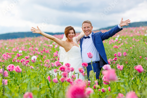 Happy wedding couple in pink poppy field