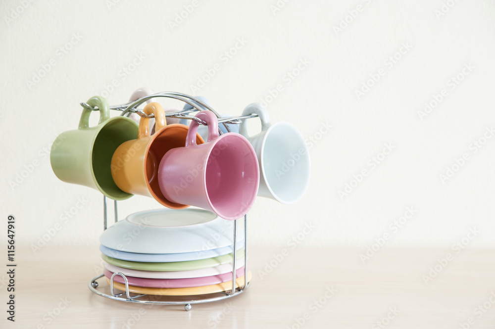 Pile of colorful coffee cups on wooden table with cream background.