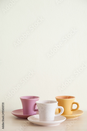 Pile of colorful coffee cups on wooden table with cream background. Top space frame.