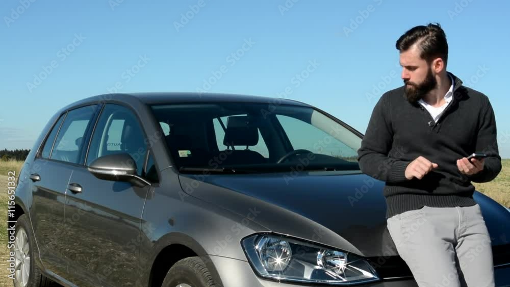 young smart handsome man work with smartphone and observe car condition of his car - he stand before car in the countryside young smart handsome man work with smartphone and observe car condition of his car - he stand before car in the countryside