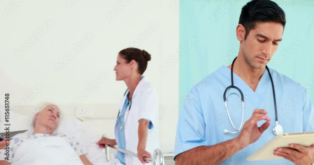 Doctor looking using tablet computer while his colleagues speaking with patient Doctor looking using tablet computer while his colleagues speaking with patient