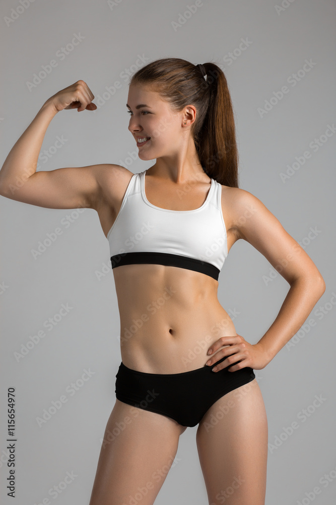 Tough young woman standing on grey background. Muscular female looking at camera. bodybuilder wearing gloves ready for gym exercise. Tough young woman standing on grey background. Muscular female looking at camera. bodybuilder wearing gloves ready for gym exercise.