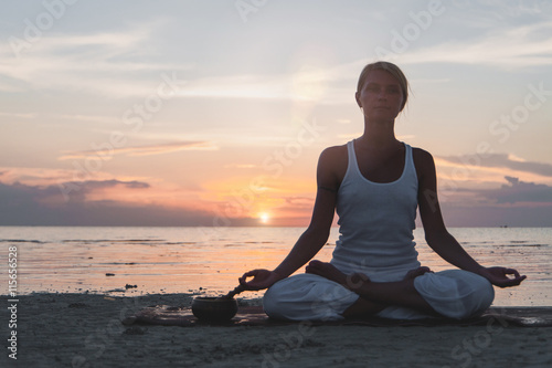 Young woman meditating at the beach at sunset