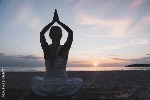 Young woman meditating at the beach at sunset