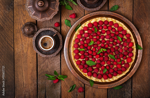 Tart with raspberries and whipped cream decorated with mint leaves on a wooden background. Top view
