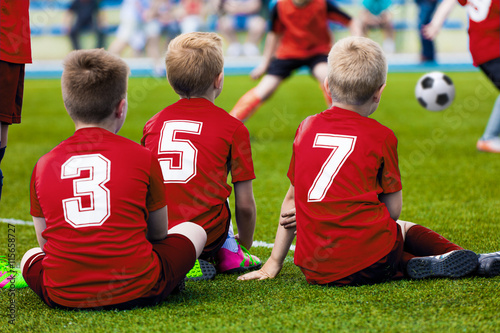 Youth soccer team on football pitch. Reserve players of red team watching soccer game and supporting team. Soccer sport tournament for elementary school teams