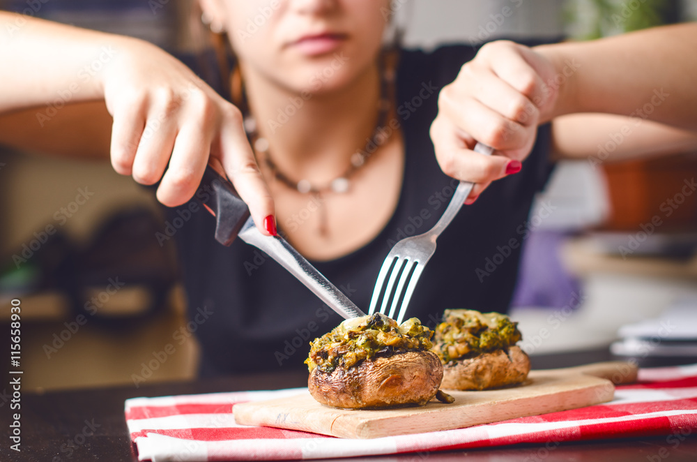 Female hands holding knife and fork and cutting meal. Mushrooms with cheese on a tablecloth. Appetizer. Food background Female hands holding knife and fork and cutting meal. Mushrooms with cheese on a tablecloth. Appetizer. Food background