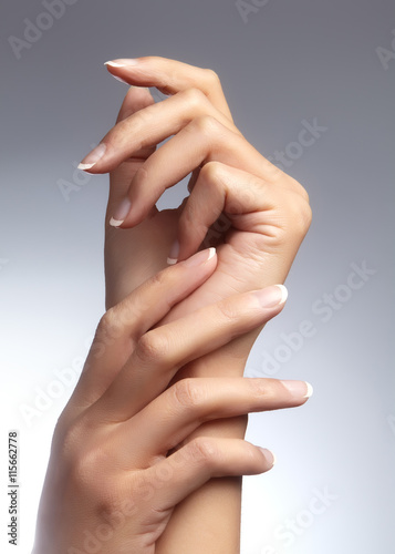 Beautiful female arms with ideal french manicure on grey background. Care about female hands, healthy soft skin. Spa & cosmetics. Beauty care.
