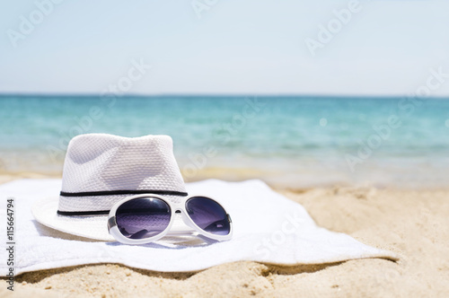 Close up of white hat and sunglasses on the beach towel as summertime concept. Beach accessories concept