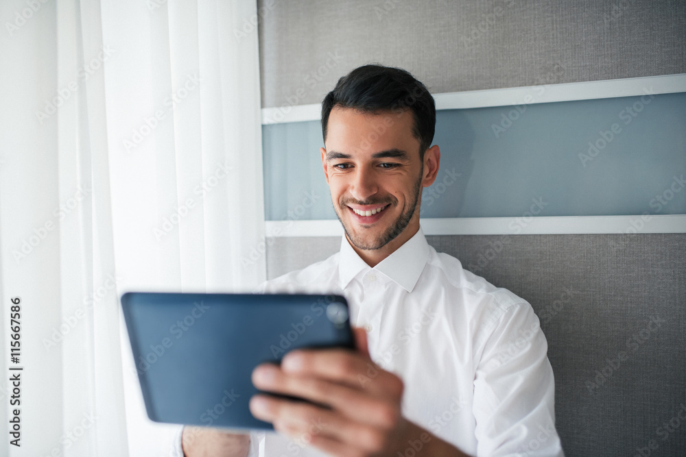 Smiling happy handsome businessman working on a device, a gadget in the office standing in front of a window. Business Smiling happy handsome businessman working on a device, a gadget in the office standing in front of a window. Business