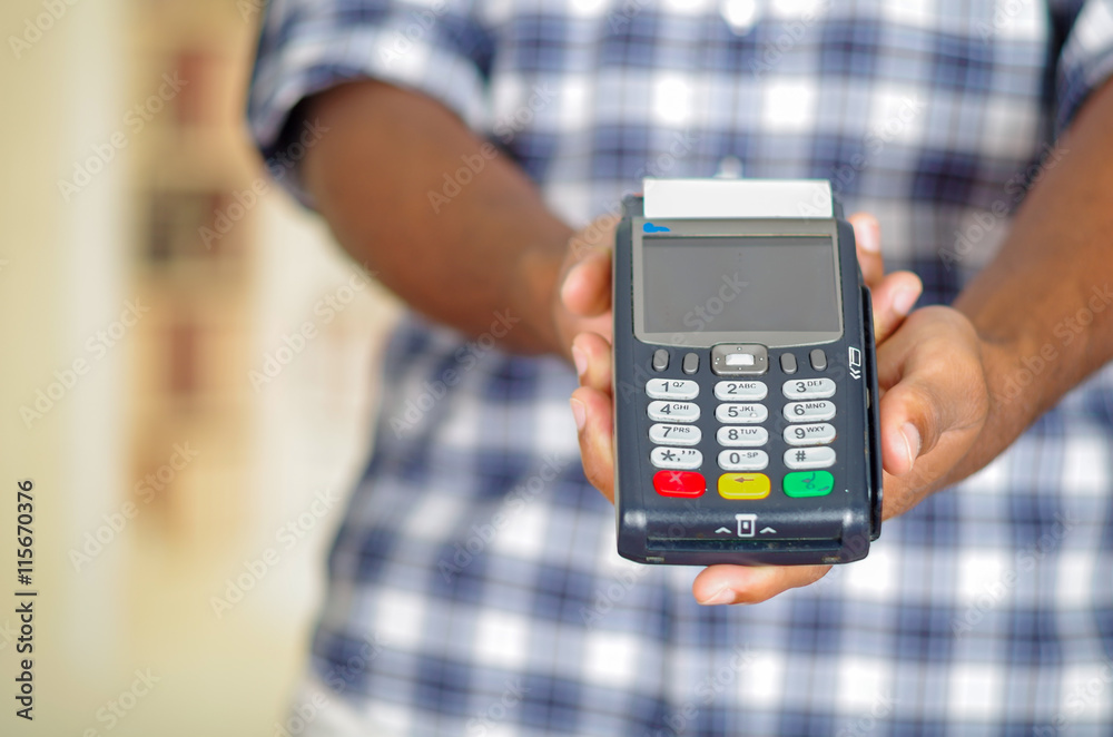 Man wearing blue white square pattern shirt holding up credit card payment terminal in front of camera Man wearing blue white square pattern shirt holding up credit card payment terminal in front of camera