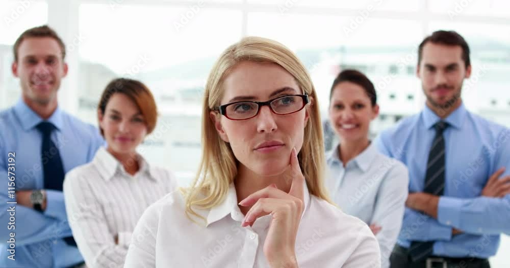 Businesswoman looking at camera with colleagues behind her in the office Businesswoman looking at camera with colleagues behind her in the office