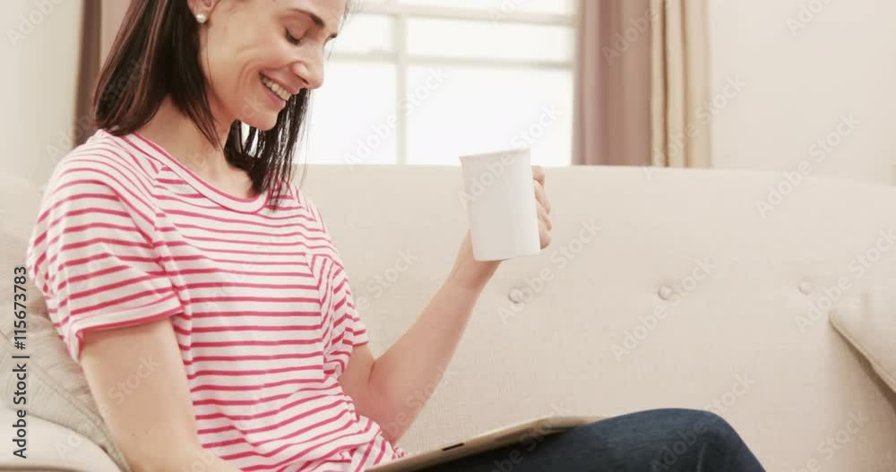 Smiling brunette drinking a coffee while watching tablet Smiling brunette drinking a coffee while watching tablet