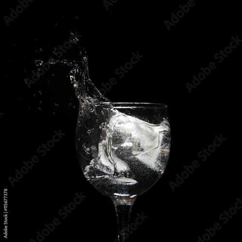 Water splash with ice in glass on black