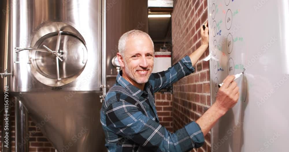 Smiling brewery worker writing notes on whiteboard Smiling brewery worker writing notes on whiteboard