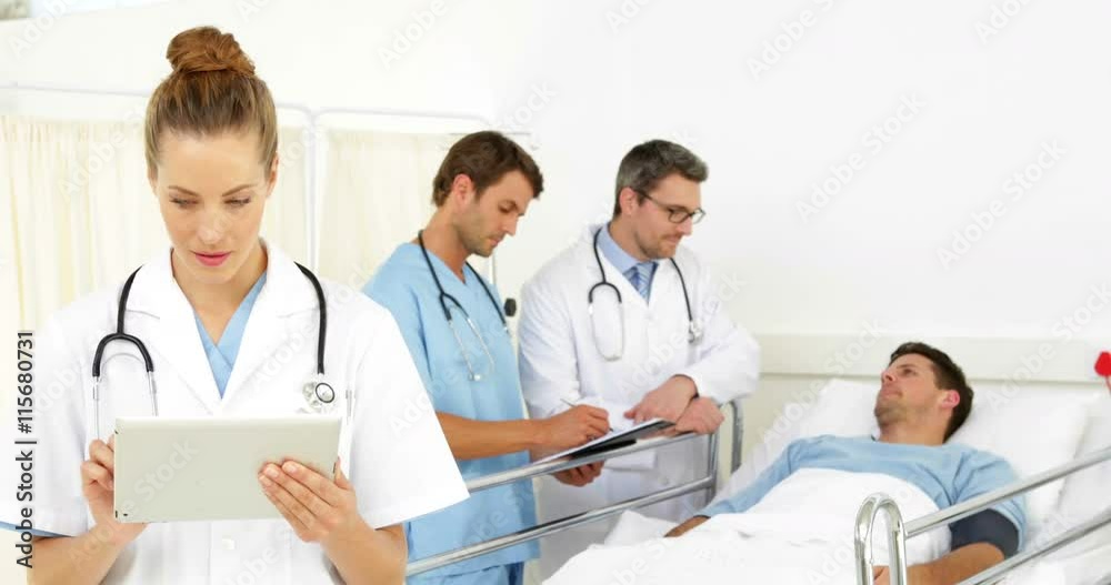 Doctors speaking with sick patient in bed while one checks tablet Doctors speaking with sick patient in bed while one checks tablet