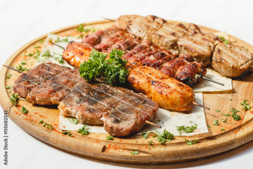 Different kind of grilled meat skewers on the wooden plate on white background