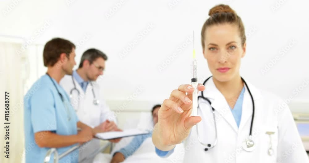 Doctors speaking with sick patient in bed while nurse prepares syringe Doctors speaking with sick patient in bed while nurse prepares syringe