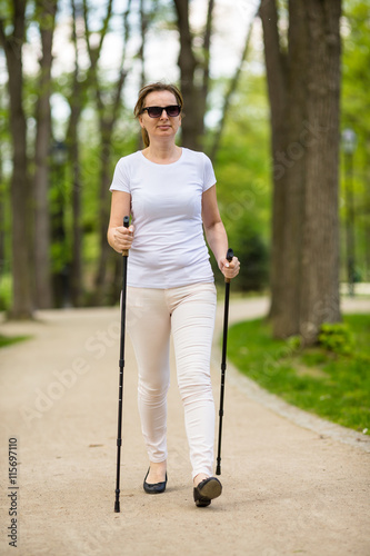 Nordic walking - middle-age woman working out in city park 