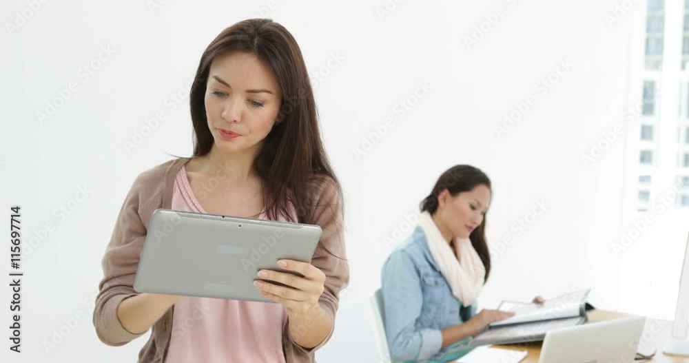 Creative businesswoman using tablet with colleague behind her Creative businesswoman using tablet with colleague behind her