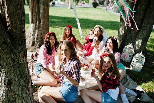 Seven happy and sexy girls sitting at picnic table and eating st