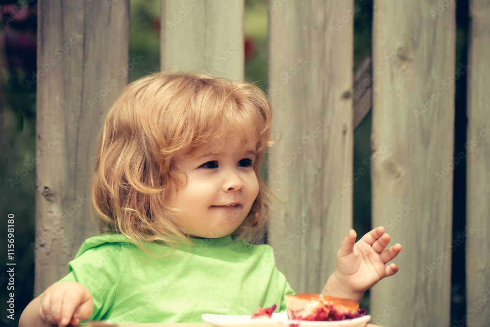 Fototapeta premium small boy eating pie near wooden fence