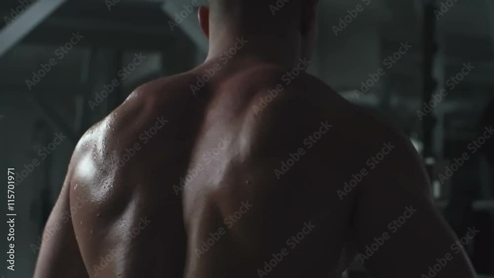 Rear view of man with naked sweating back doing side raise with dumbbells