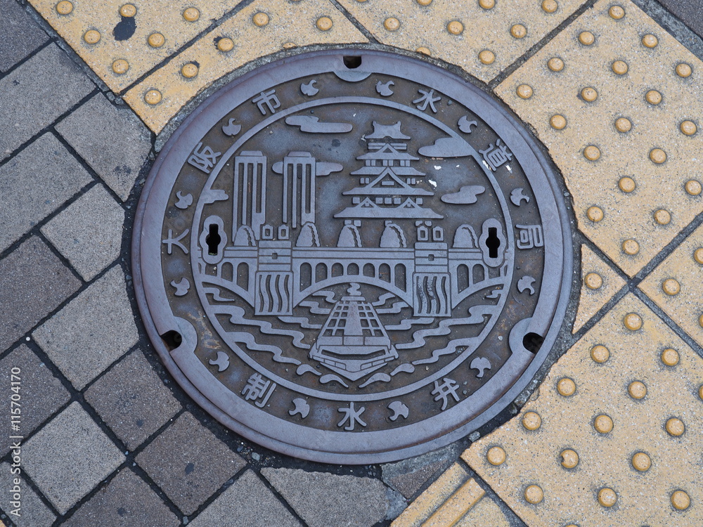 A manhole cover in Osaka, Japan. A ship on Dotonbori canal and Osaka castle engraved on to a manhole cover as a symbol of an important city's landmark.