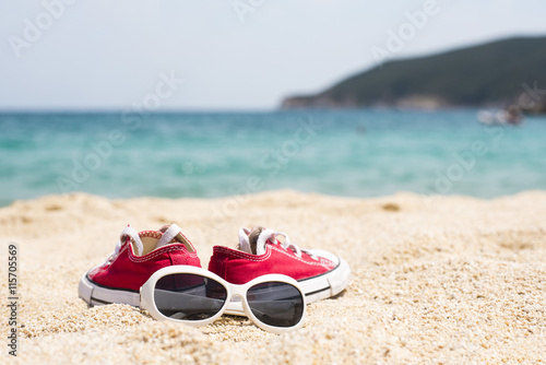 Close up of sunglasses and red sneakers on the beautiful sand beach as summertime concept