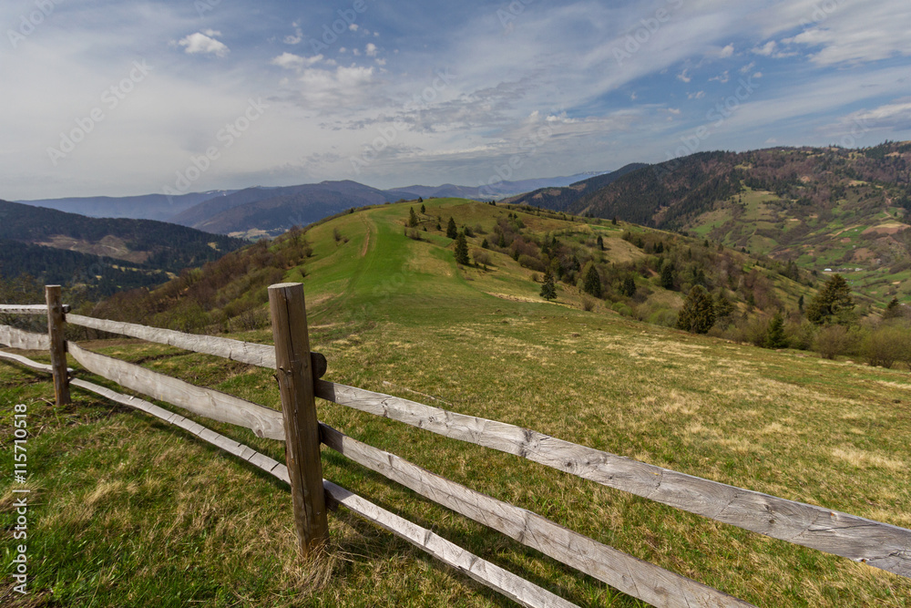 Pasture in mountains and a wooden fence in the foreground. Carpa