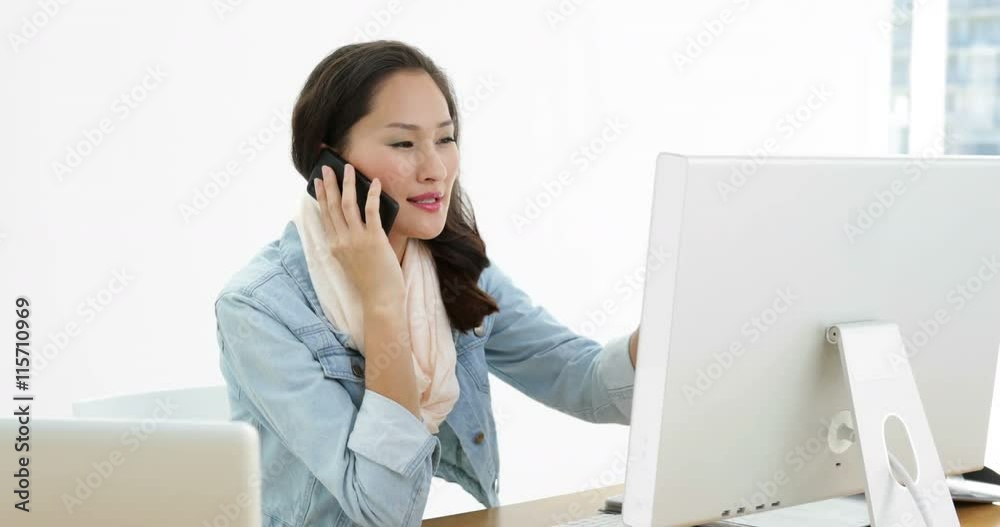 Asian woman working at desk using computer talking on the phone Asian woman working at desk using computer talking on the phone