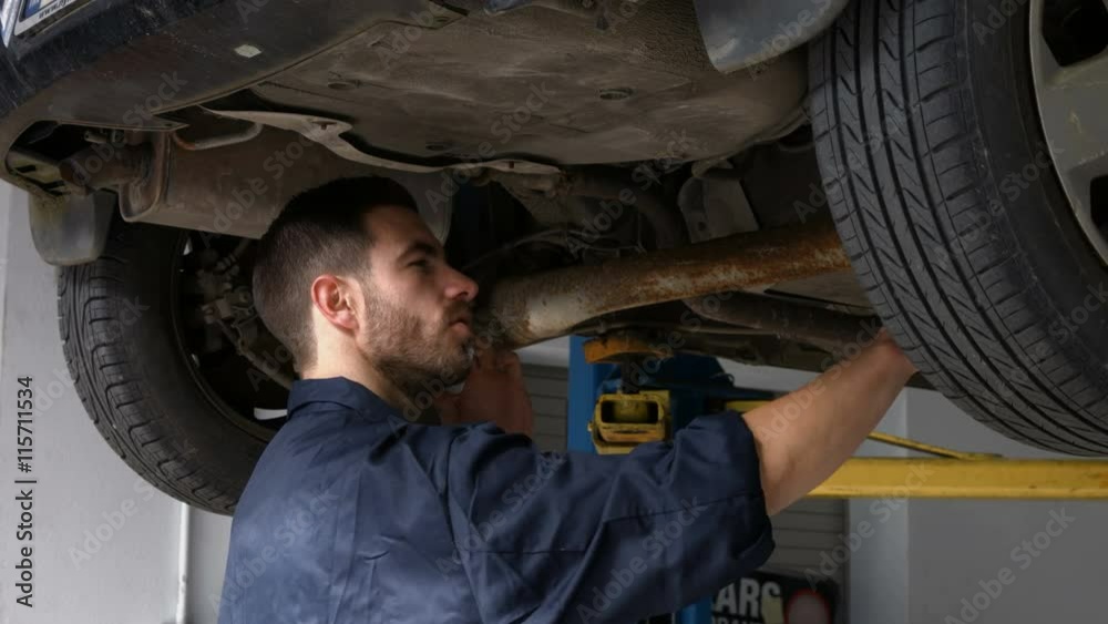 Handsome mechanic overhauling a car while having a phone call in his garage Handsome mechanic overhauling a car while having a phone call in his garage