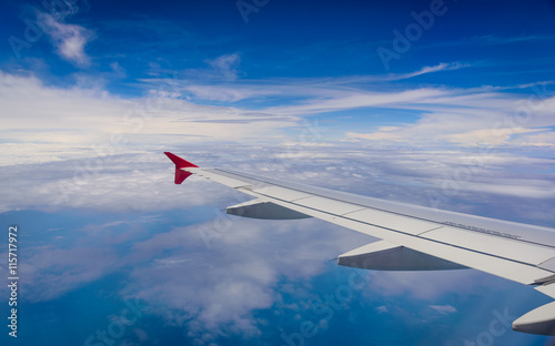 Wing of airplane flying above the clouds in the blue sky backgro