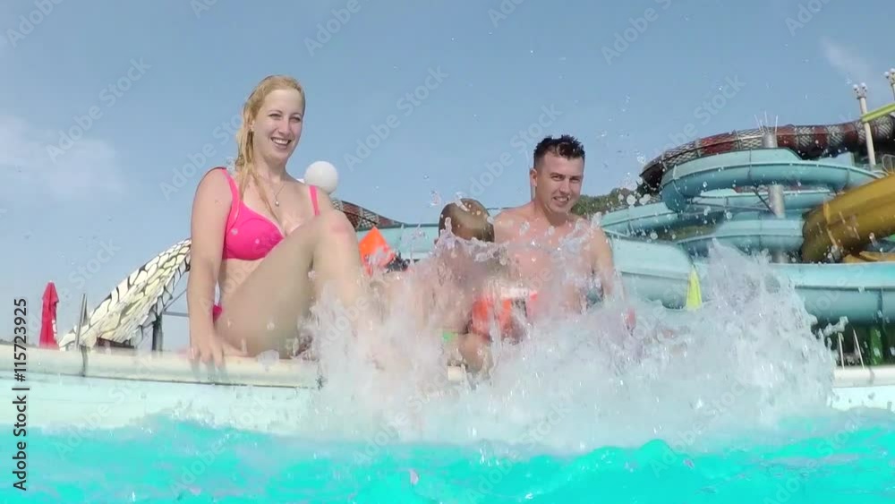 SLOW MOTION: Happy young family splashing pool water into camera SLOW MOTION: Happy young family splashing pool water into camera