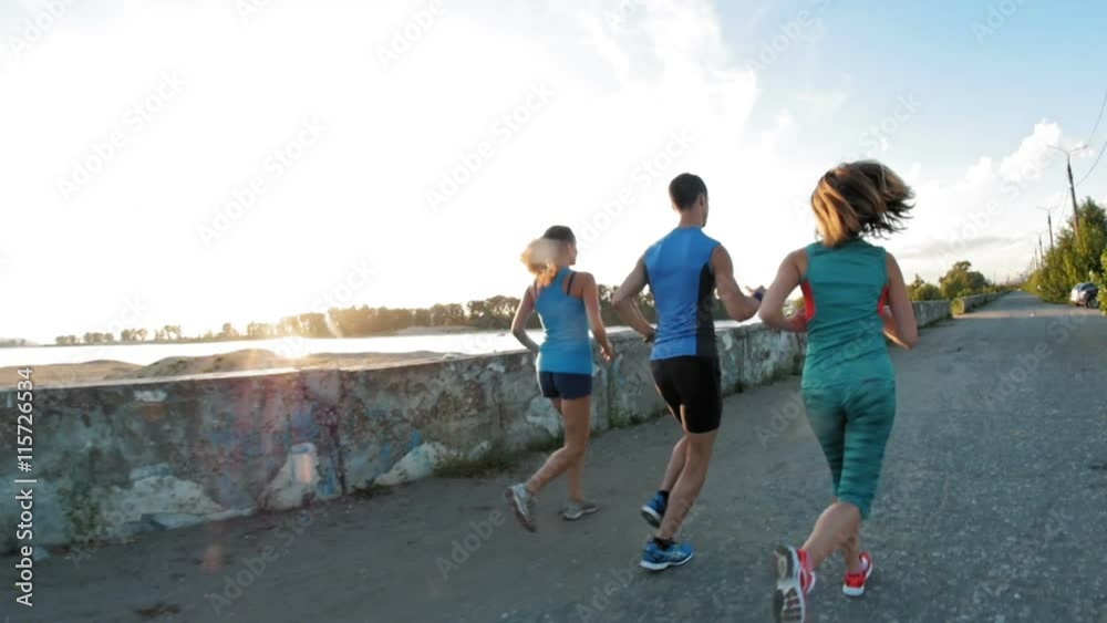 A group of athletes - two girls and a guy running at city park, near river at sunset, slow-motion A group of athletes - two girls and a guy running at city park, near river at sunset, slow-motion