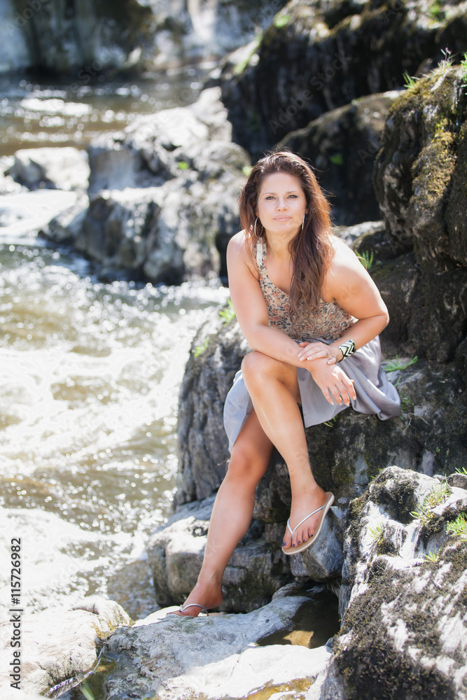 Beautiful young lady sat on rocks by a river