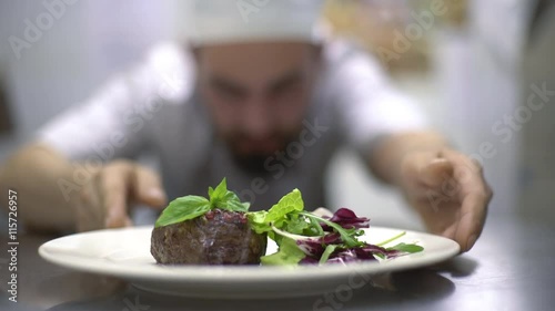 Chef is finishing meal teasty beef steak with salad for guest of restaurant. Final touch basil leaf photo